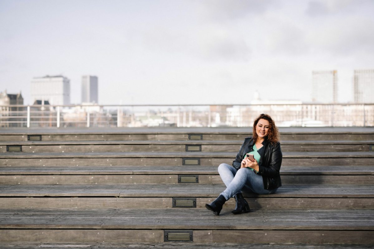 Claudia Voogt zit op een trap met de skyline van Rotterdam